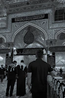 Devout pilgrims performing ziarat in the holy sites of Karbala, framed by intricate Islamic architectural details.