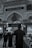 An ornate interior features detailed Arabic calligraphy and decorative arches. People wearing black clothing, some with keffiyehs, walk on a patterned carpet. The scene reflects a solemn and reverent atmosphere.