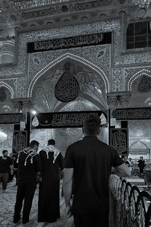 Devout pilgrims performing ziarat in the holy sites of Karbala, framed by intricate Islamic architectural details.