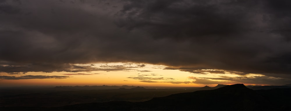 the sun is setting over the mountains with dark clouds