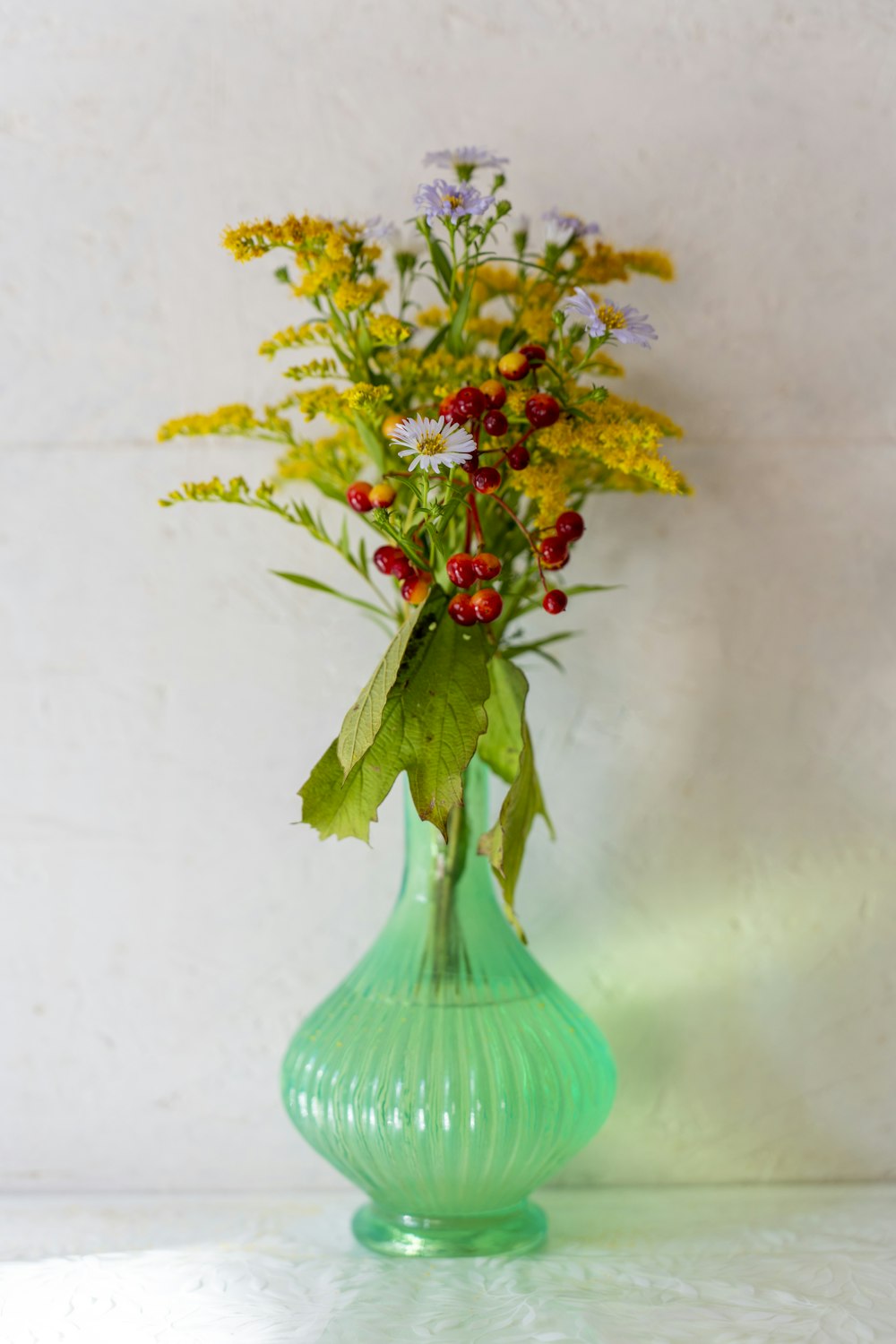 a green vase filled with lots of colorful flowers