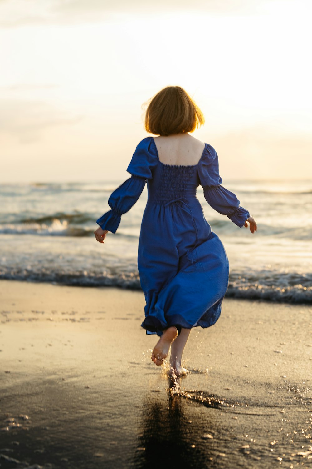 Una donna in un vestito blu che corre sulla spiaggia