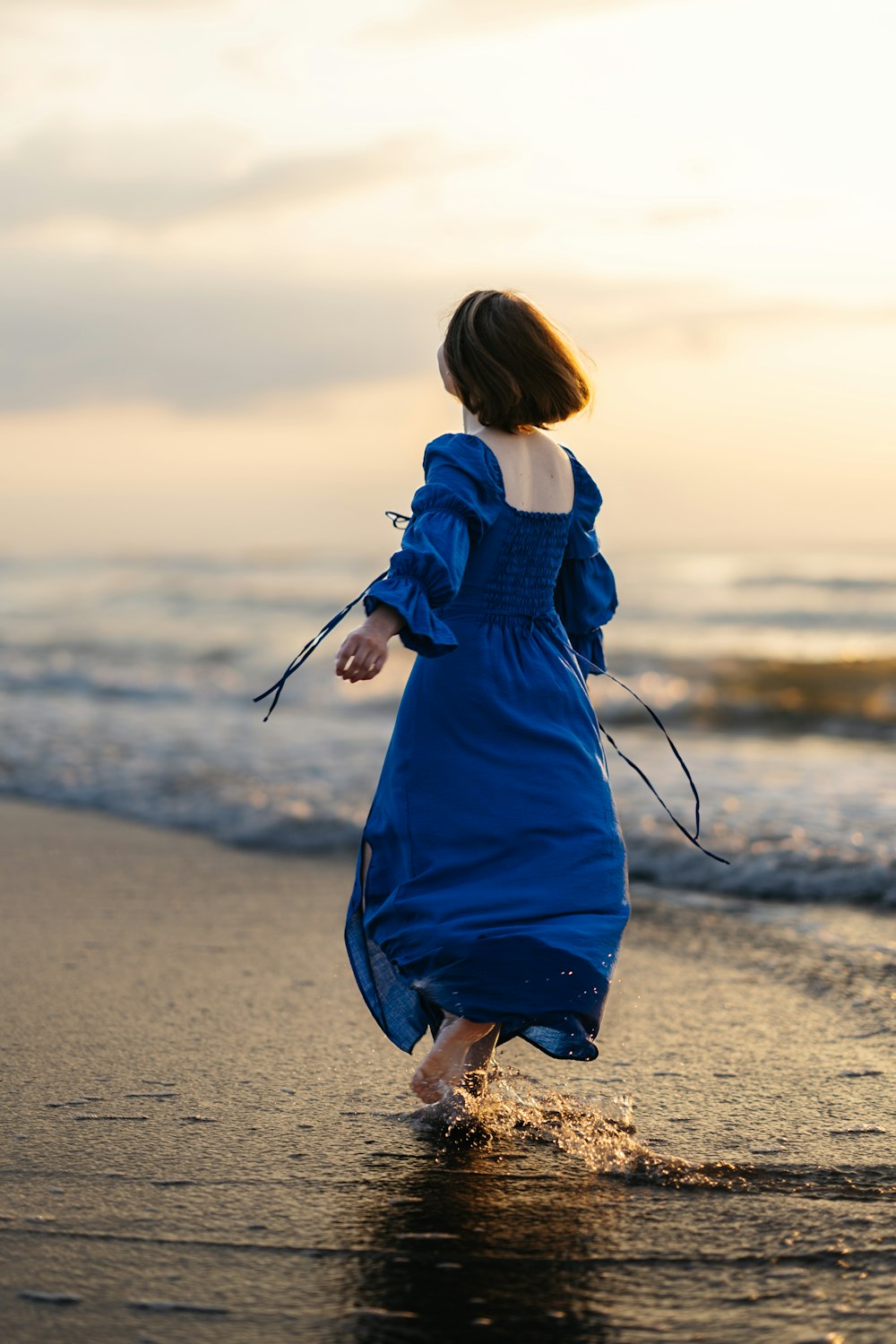 a woman in a blue dress walking on the beach