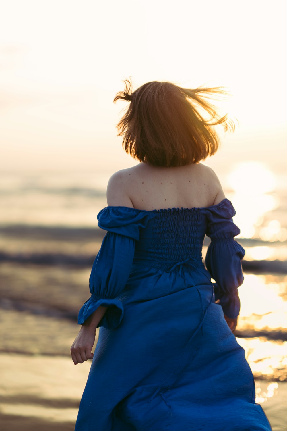 a woman in a blue dress walking on the beach