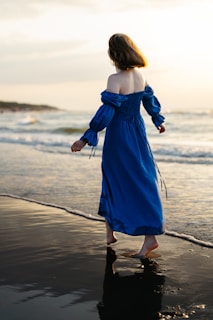 A model walking along the shore wearing a soft pink beach cover-up that flows gently in the breeze under a pastel sunset.