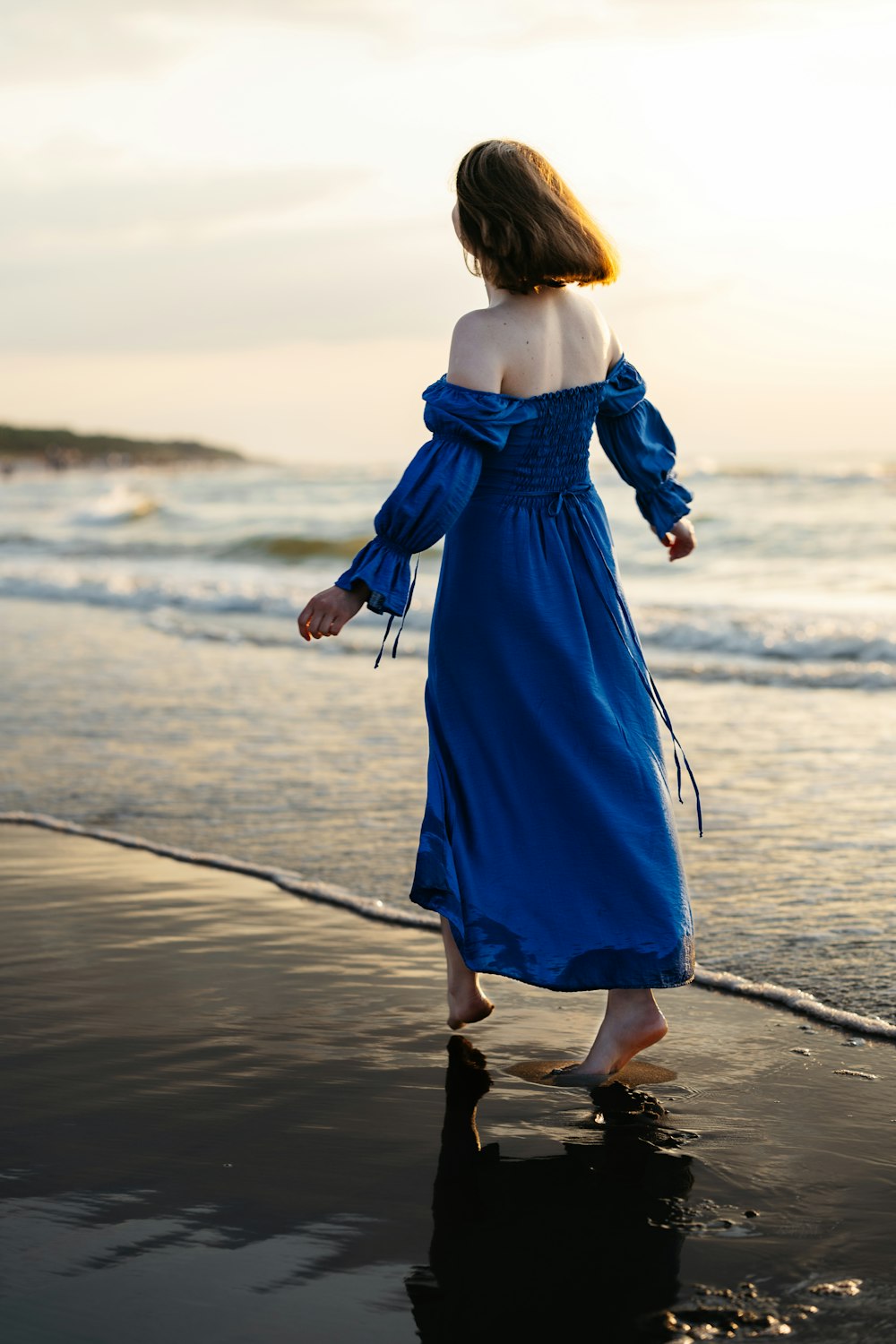 a woman in a blue dress walking on the beach