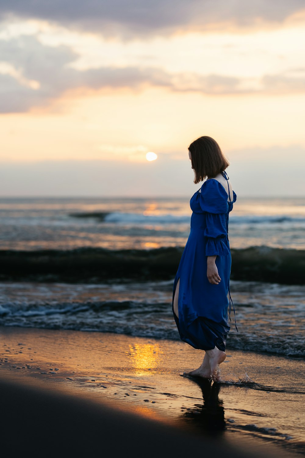 a woman in a blue dress is walking on the beach