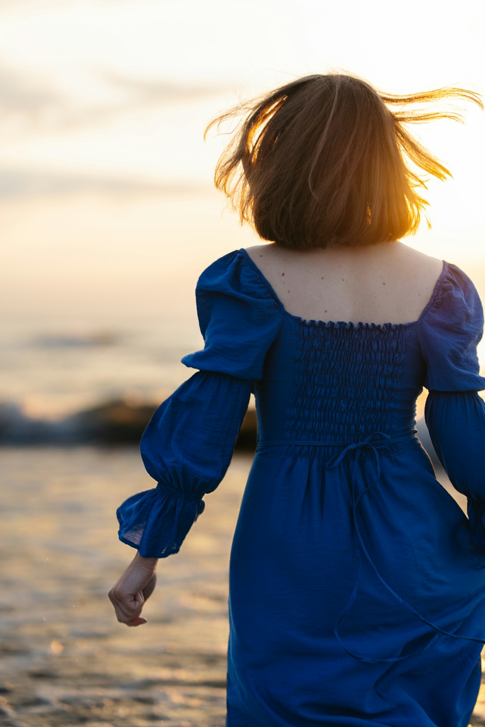 a woman in a blue dress walking on the beach