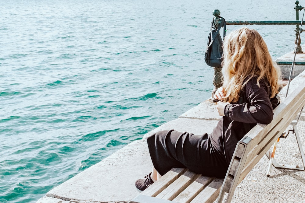 a woman sitting on a bench next to a body of water