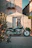 Close-up of a lightweight adventure bike parked beside a whitewashed village street lined with olive trees.