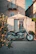 Close-up of a lightweight adventure bike parked beside a whitewashed village street lined with olive trees.