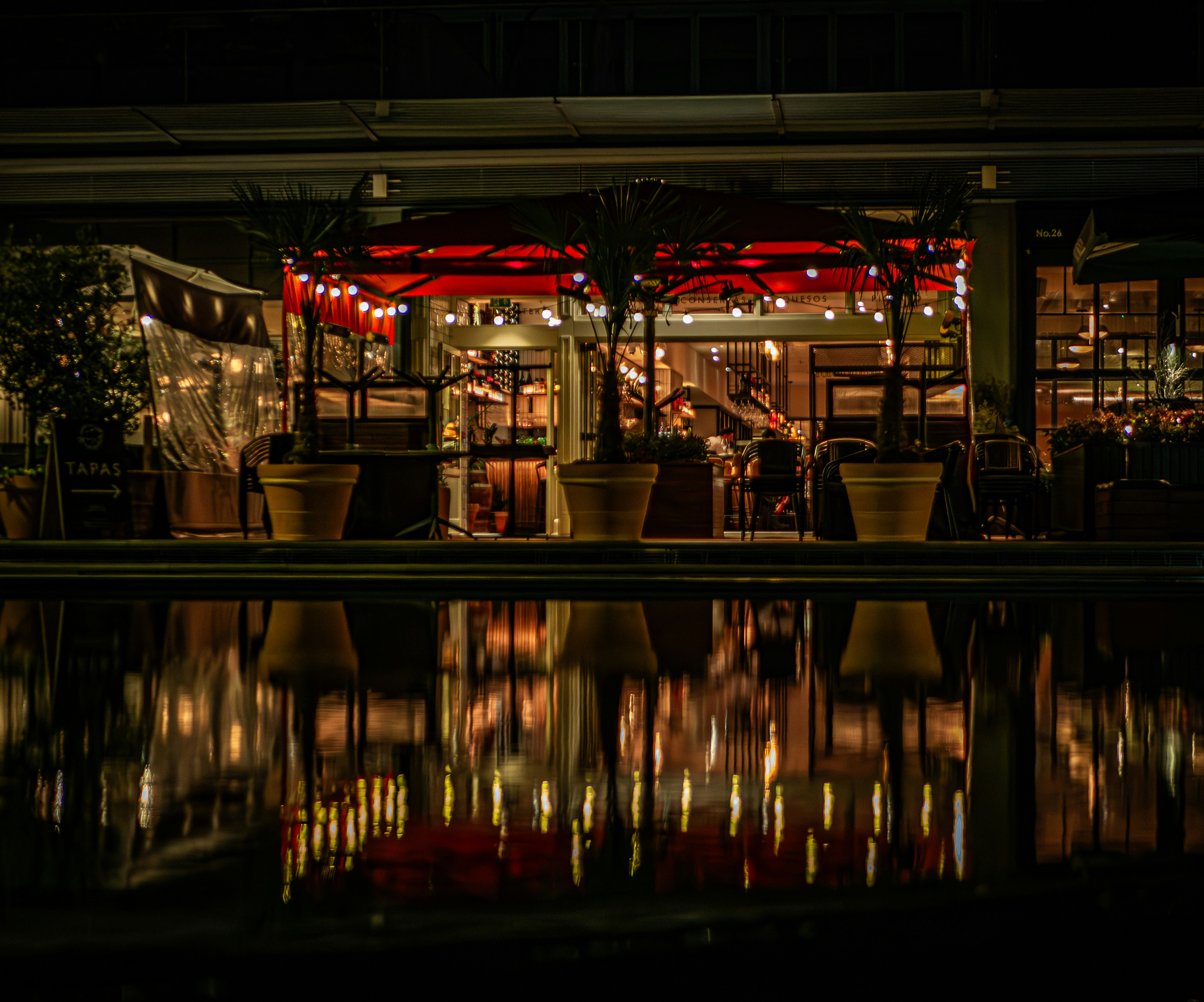 a restaurant is lit up at night with lights reflecting in the water, 