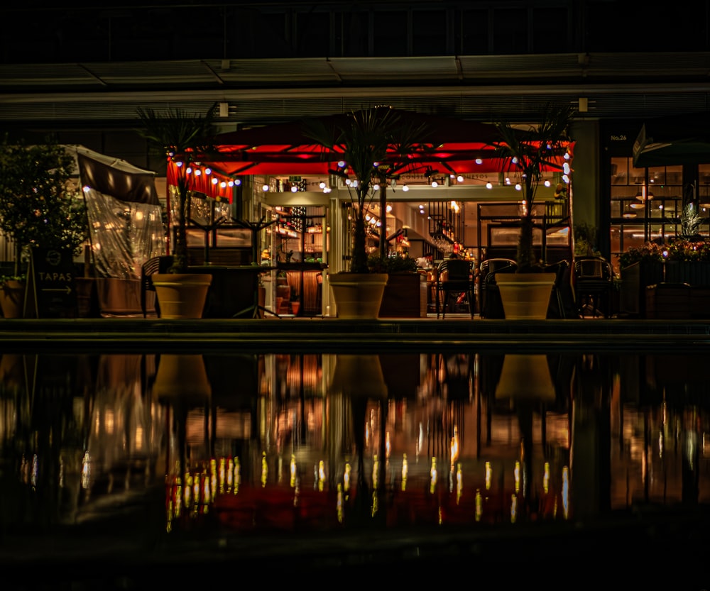 a restaurant is lit up at night with lights reflecting in the water