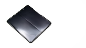 A sleek, foldable smartphone with a glossy screen lies partially unfolded on a plain white surface, highlighting its modern design and technology.