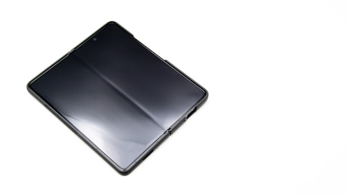 A sleek, foldable smartphone with a glossy screen lies partially unfolded on a plain white surface, highlighting its modern design and technology.