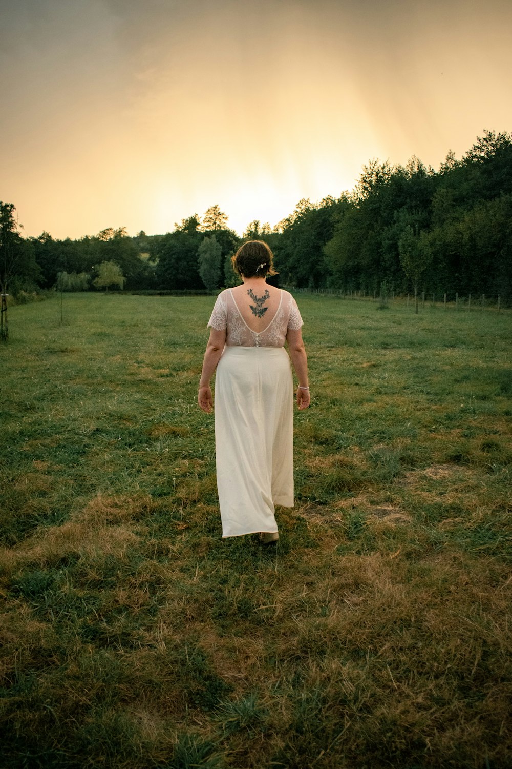 a woman in a white dress walking through a field