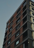 A high-rise building with a modern design, featuring a mix of brick and concrete facades. The structure includes multiple stories with uniform, rectangular windows, and visible balconies with metal railings.