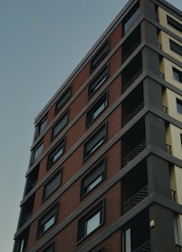 A high-rise building with a modern design, featuring a mix of brick and concrete facades. The structure includes multiple stories with uniform, rectangular windows, and visible balconies with metal railings.