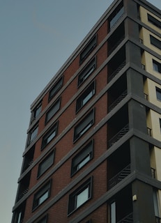 A high-rise building with a modern design, featuring a mix of brick and concrete facades. The structure includes multiple stories with uniform, rectangular windows, and visible balconies with metal railings.