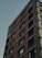 A high-rise building with a modern design, featuring a mix of brick and concrete facades. The structure includes multiple stories with uniform, rectangular windows, and visible balconies with metal railings.
