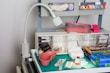 A medical supply cart featuring an adjustable lamp, various medical containers, and supplies organized neatly. Items include pink kidney trays, a container with gloves, rolls of tape, gauze pads, a pair of scissors, and bottles of medical liquids. The cart also holds boxes labeled for gloves and other medical essentials.
