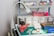 A medical supply cart featuring an adjustable lamp, various medical containers, and supplies organized neatly. Items include pink kidney trays, a container with gloves, rolls of tape, gauze pads, a pair of scissors, and bottles of medical liquids. The cart also holds boxes labeled for gloves and other medical essentials.