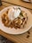 A plate of waffles topped with sliced bananas, a generous drizzle of caramel sauce, and a scoop of vanilla ice cream, garnished with a mint leaf. The plate is set on a wooden table, creating a warm and inviting atmosphere.