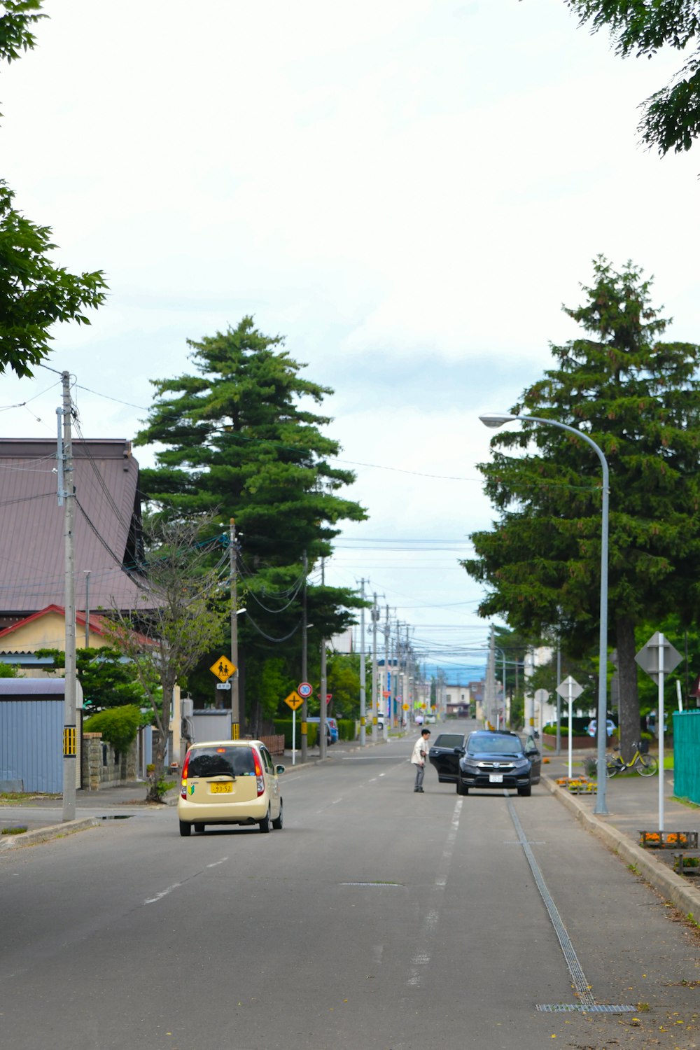 a yellow car driving down a street next to tall trees