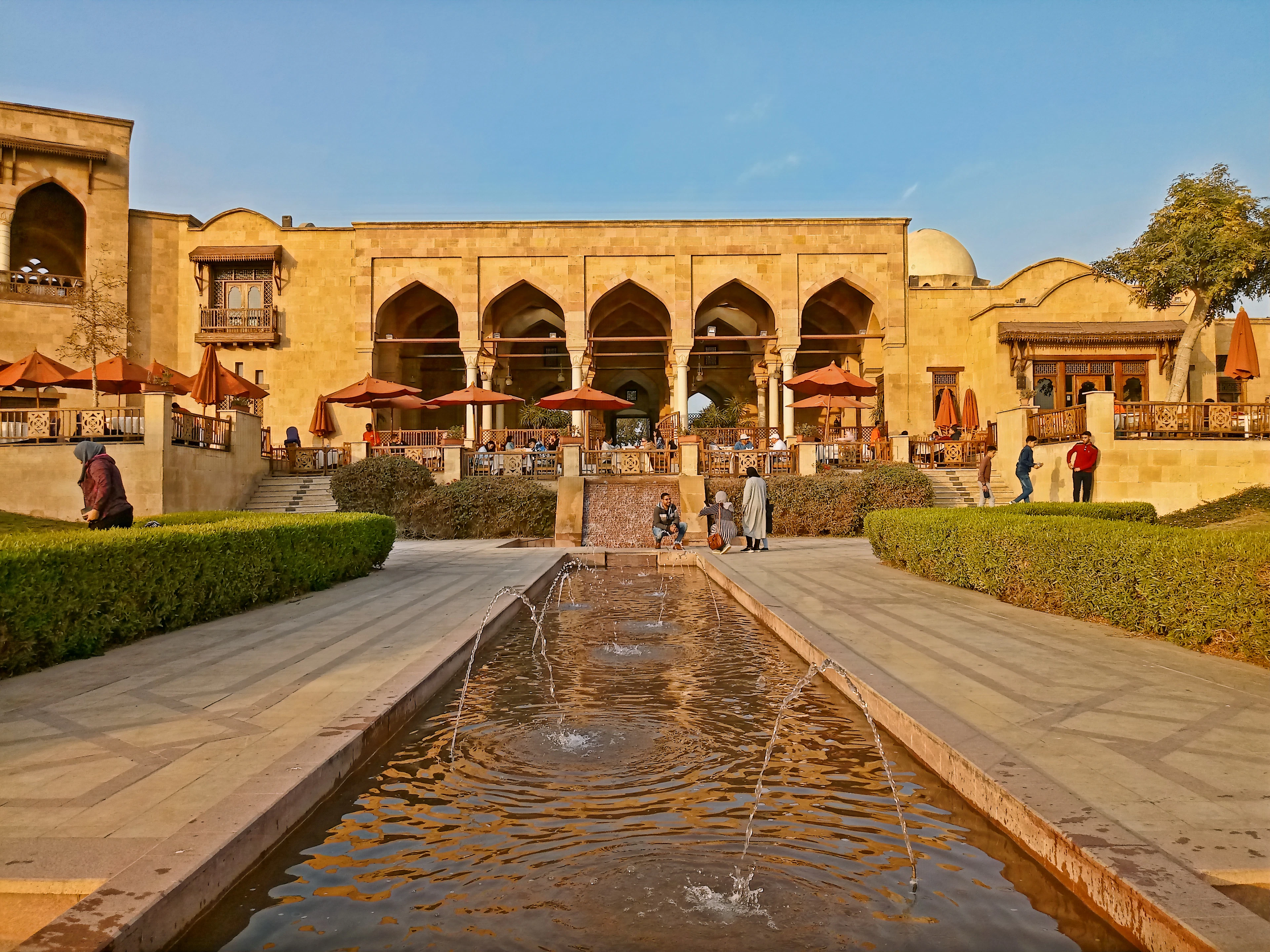 Fountains jet from a long reflecting pool before a golden-lit stone pavilion in Al-Azhar Park.