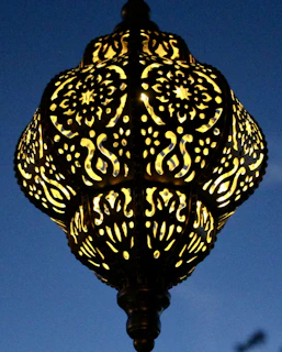 Close-up of a handcrafted lamp with traditional Indian motifs glowing warmly on a wooden side table