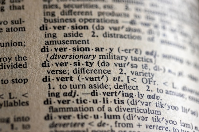 A close-up view of a dictionary page showing words and definitions related to 'diversion' and 'diversity'. The text is crisp with clear phonetic transcription and explanations in a serif font. The paper has a textured, off-white appearance, suggesting age or frequent use.