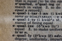 A close-up view of a dictionary page displaying the word 'equality' with its pronunciation and definition emphasized in bold text. The page shows the word's usage in different forms and sentences, with some words italicized to denote emphasis, all printed on aged, slightly yellowed paper.