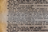 Close-up view of a dictionary page featuring the entry for the word 'environment,' including its pronunciation, definition, and related terms such as 'environmentalist.' The text explains the concept in detail and mentions issues like water pollution and resource use.