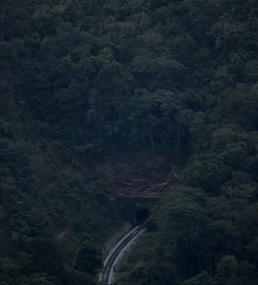 Aerial shot of a busy railway tunnel entrance nestled in lush green terrain.