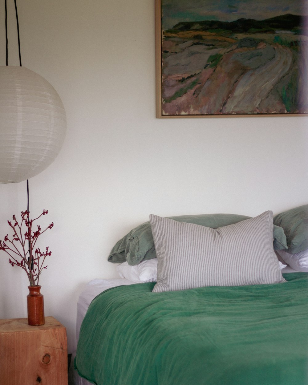 a bed with a green comforter and a painting on the wall