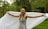 A young person with braided hair is joyfully holding a large white sheet in a lush green forest. The trees and foliage in the background create a serene natural setting.