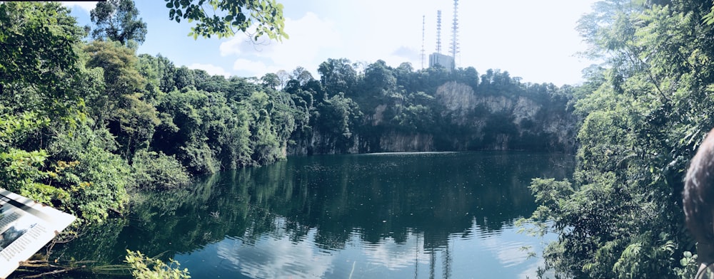 Un lago rodeado de árboles con una torre de radio al fondo