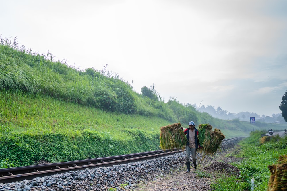 a man walking down a train track carrying a load of hay