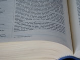 An open book with text written in English, with a focus on a specific page. The text appears to be part of a religious or spiritual scripture, containing paragraphs with chapter and verse numbers.
