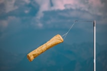 A yellow windsock extends horizontally from a metallic pole against a backdrop of a cloudy sky, indicating a windy day.