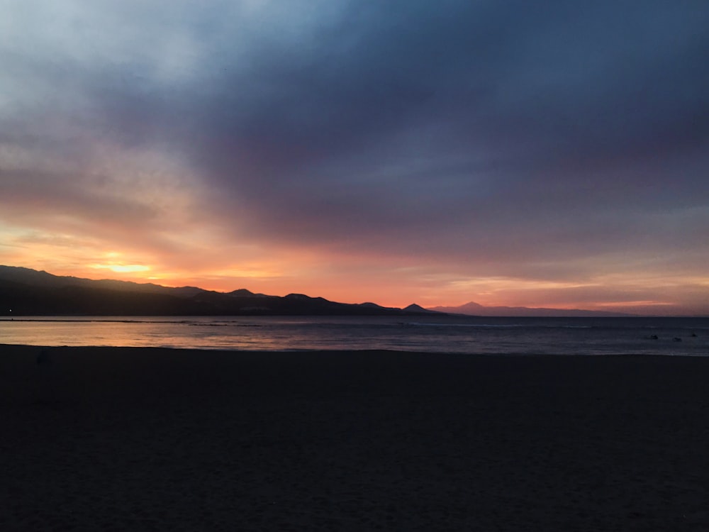 the sun is setting over a beach with mountains in the distance