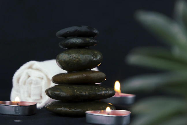 Close-up of rolled towels and a small bowl of smooth stones on a spa table under soft lighting.