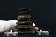 Stacked smooth black stones beside a lit candle and fresh lavender sprigs.