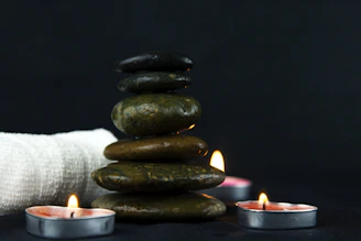 Smooth heated stones arranged artfully on a wooden tray beside aromatic candles.