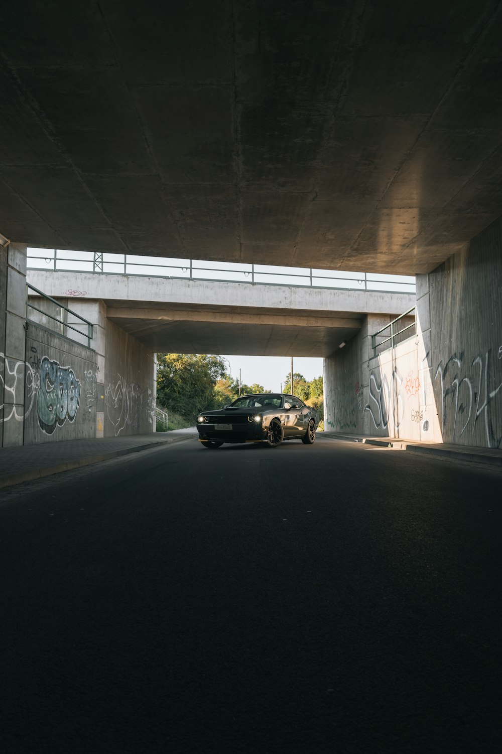 a car driving under a bridge with graffiti on it