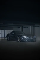 Side view of a sleek black sports car with a glossy new paint job under bright garage lights.