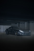 A sleek black sports car with a glossy finish parked in front of a modern garage at sunset.