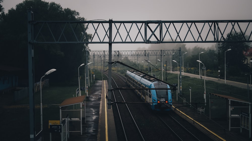 a blue train traveling down train tracks next to a forest