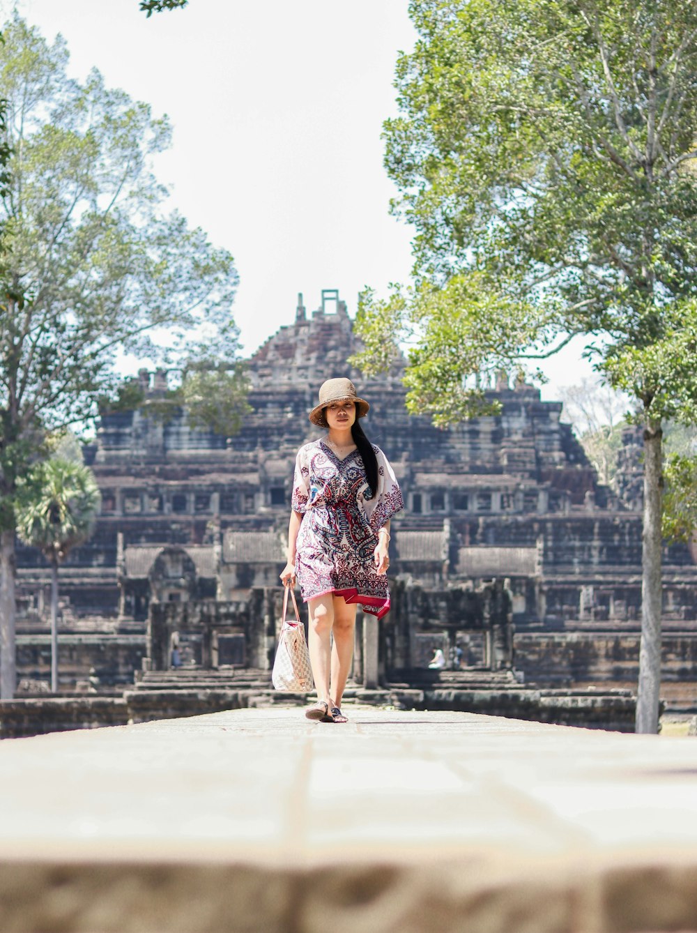 a woman in a hat and dress walking down a sidewalk