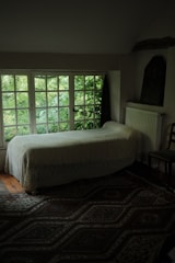 A warmly lit guest room with a comfortable bed, soft pillows, and a window showing greenery outside.